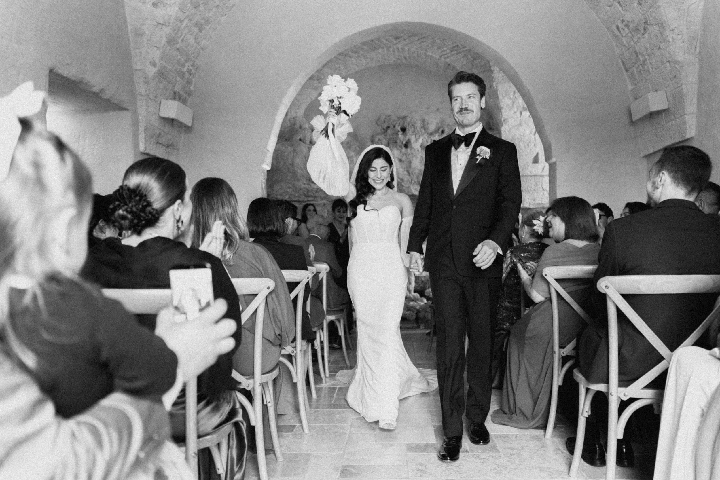 Bride and groom walk down the aisle together after wedding ceremony in elegant stone chapel.