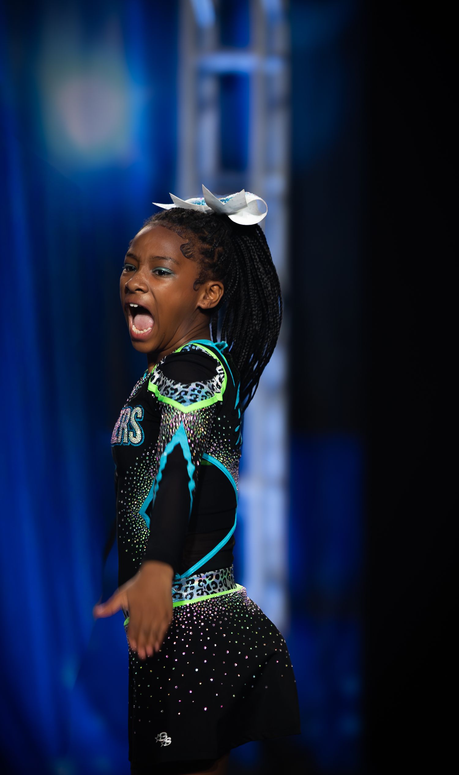 Young cheerleader in Panthers uniform performing energetically on stage at a cheerleading competition.