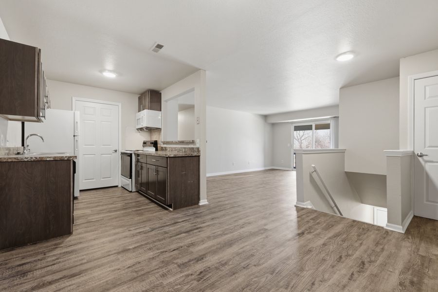 Open kitchen and living area with dark wood cabinets, granite island, and light hardwood floors.