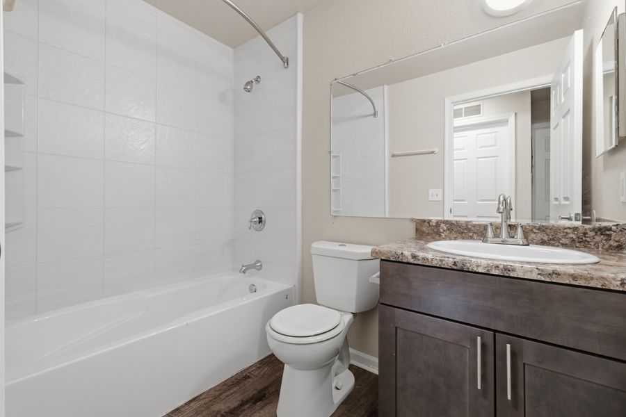 Modern bathroom with white tiled tub-shower combo, toilet, and dark wood vanity with granite countertop.