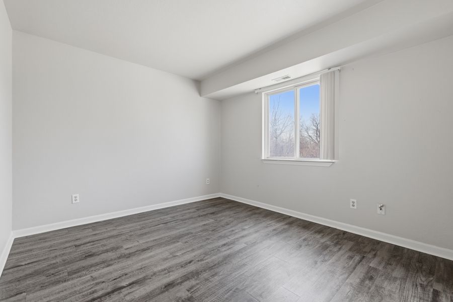 Bright empty bedroom with dark hardwood floors, white walls, and a single window with natural light.