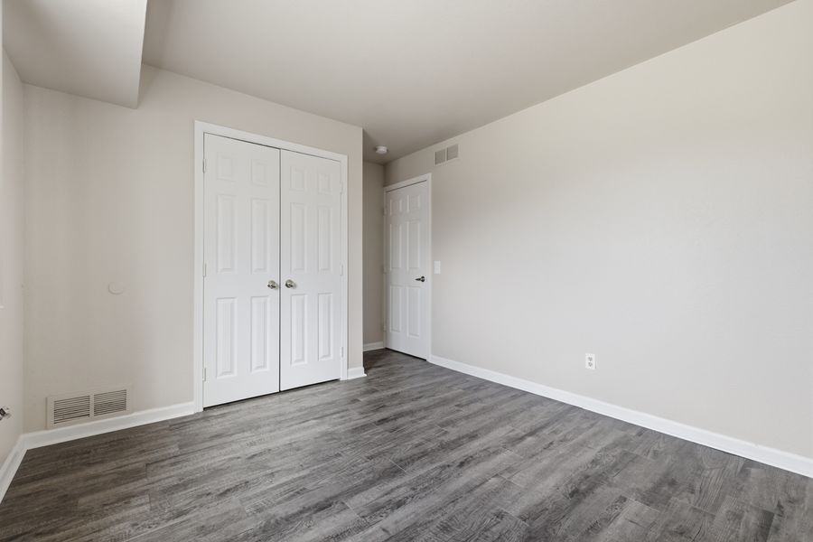 Empty bedroom with dark hardwood floors, white walls, double closet doors, and a single door.