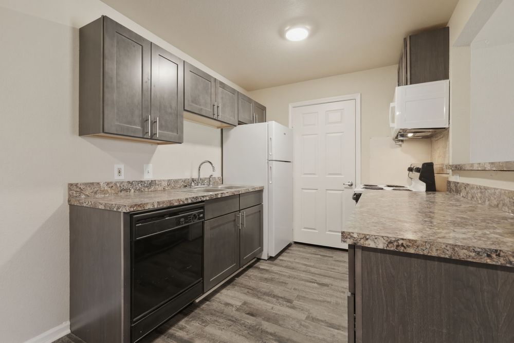 Modern kitchen with dark gray cabinets, granite countertops, black dishwasher, and white refrigerator.
