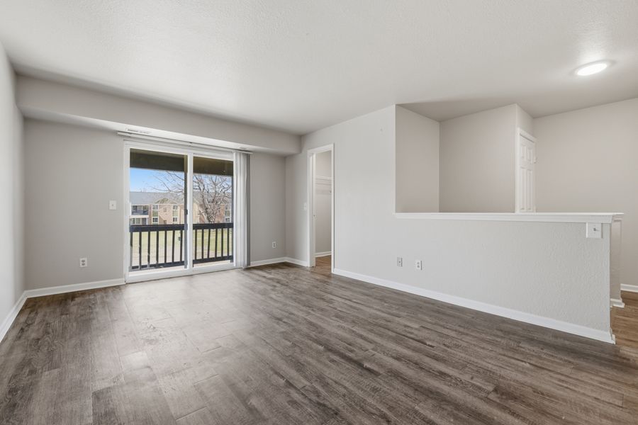 Bright empty living room with hardwood floors, sliding glass door, and balcony access.
