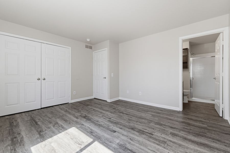 Spacious bedroom with gray hardwood floors, double closet doors, and an en-suite bathroom visible through open doorway.