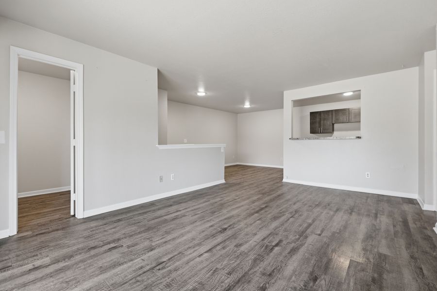 Spacious empty living room with dark hardwood floors and open pass-through to kitchen.