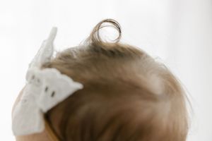 Close-up of a baby's head with a tiny hair curl and white lace bow headband.