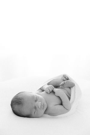 Black and white photo of a peaceful newborn baby sleeping curled up in a soft white wrap.