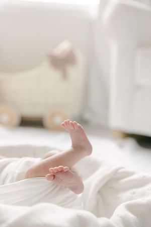 Close-up of tiny newborn baby feet peeking out from white blanket with soft toy lamb in background.