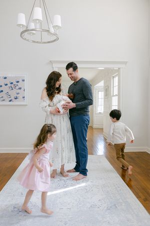 Happy family with two young children and newborn baby gathered in a bright, elegant home entryway.