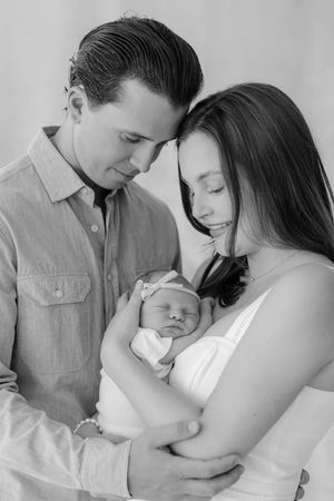 Black and white photo of new parents tenderly cradling their sleeping newborn baby.