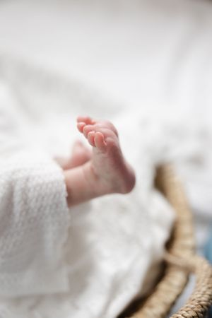 Close-up of tiny newborn baby feet peeking out from a white blanket in a woven basket.