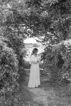 Black and white photo of a woman in a white dress standing on a garden path framed by lush trees.