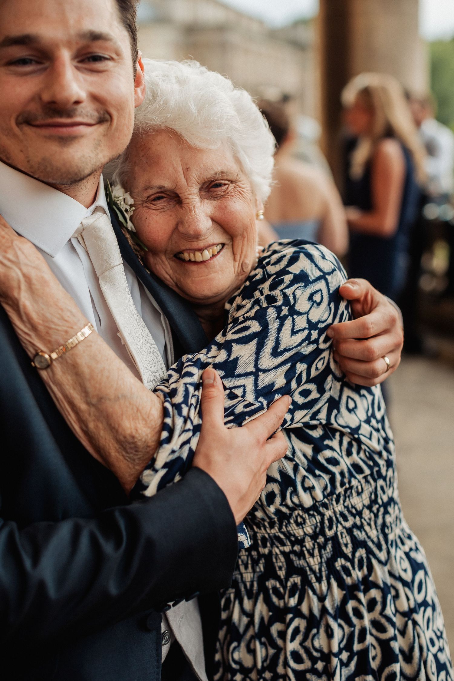 Elderly woman smiling warmly while embracing a young man in a suit at a formal event.