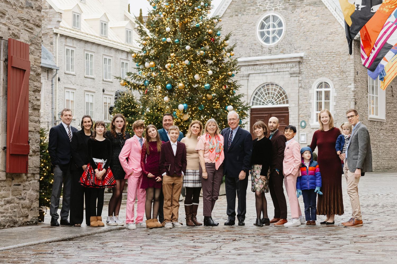 Large family group posing outdoors near a decorated Christmas tree in a festive town square setting.
