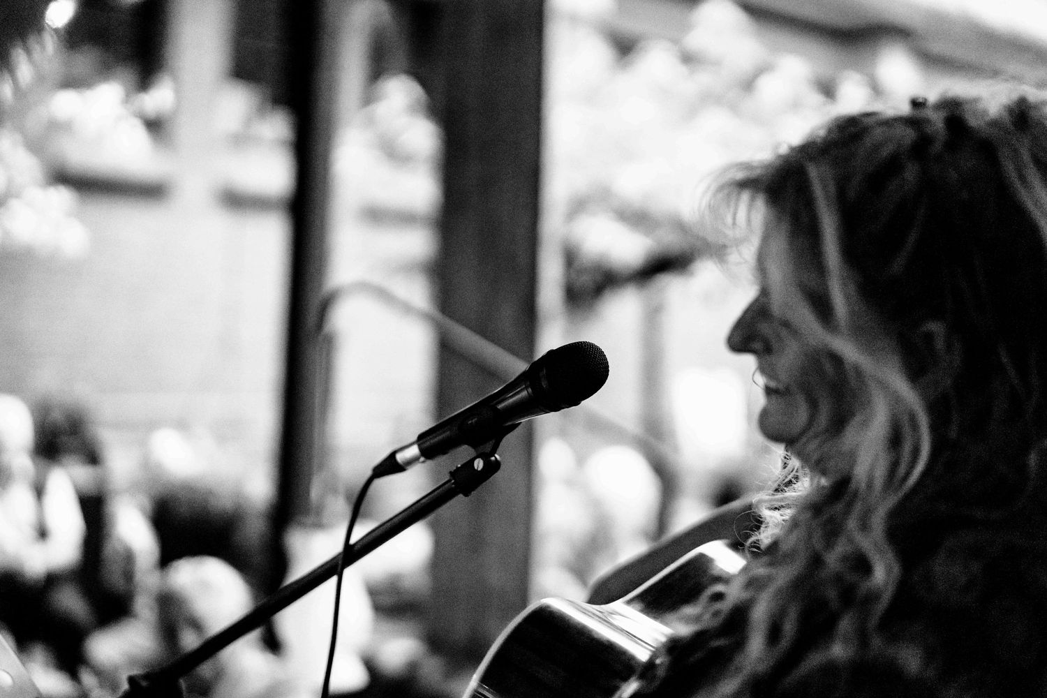 Black and white photo of a performer singing into a microphone with guitar.