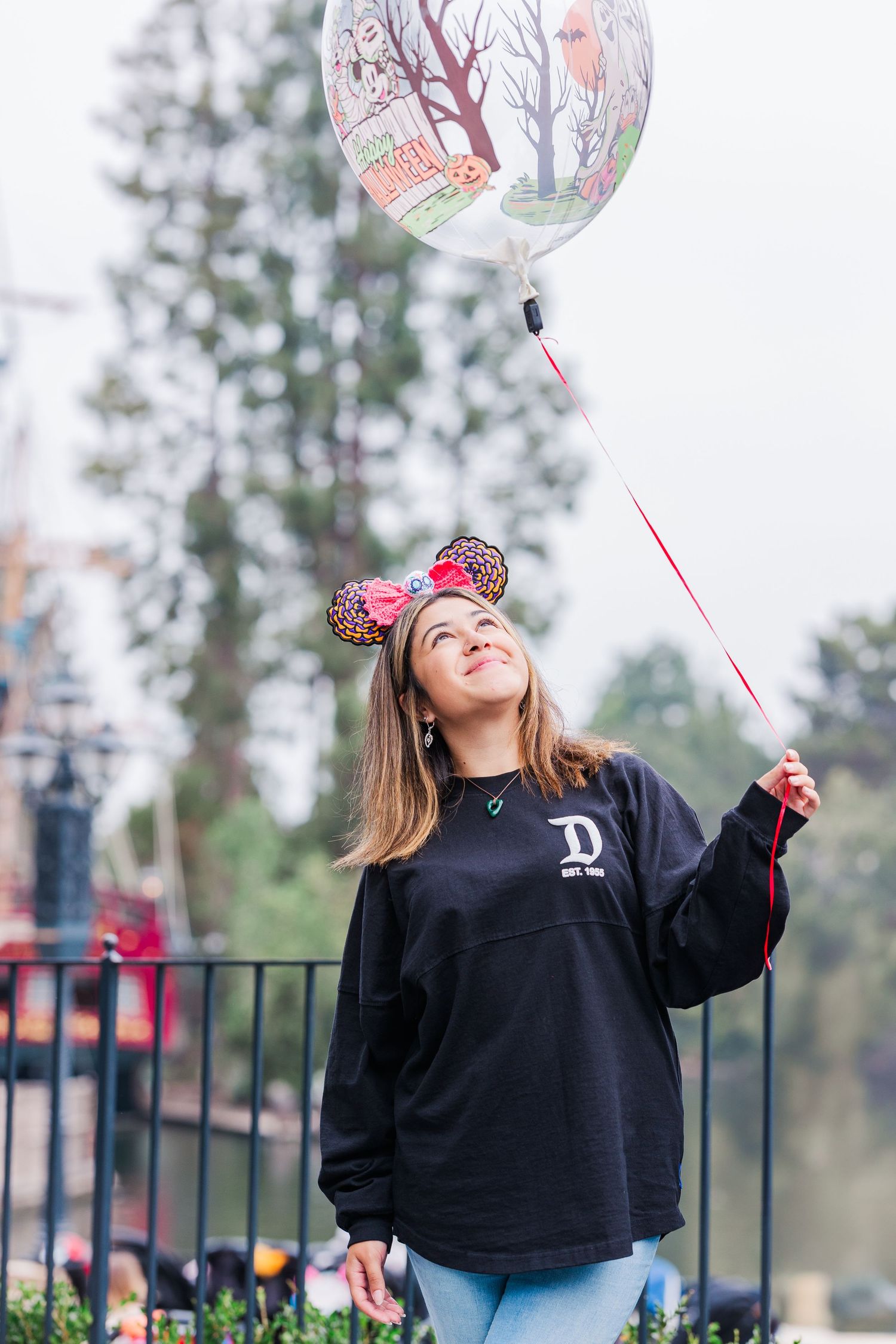 Person holding decorative balloon while wearing Disney ears and casual attire.