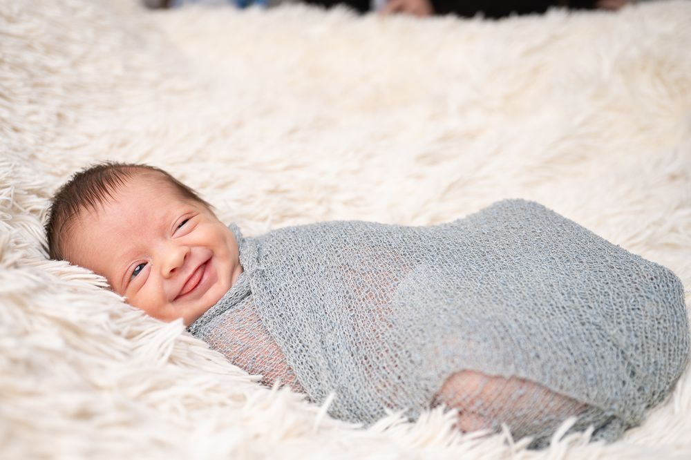 Newborn baby with sleepy face, tongue out and a cheeky grin during photoshoot at studio near Ashford, Kent.
