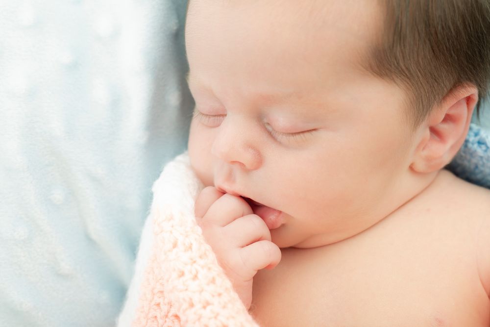 Peaceful newborn baby sleeping with hand near mouth on soft pink blanket – newborn photography studio near Ashford, Kent.