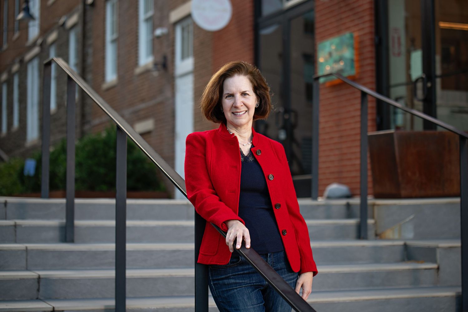 Professional portrait on brick building steps featuring person in bright red blazer and dark skirt.