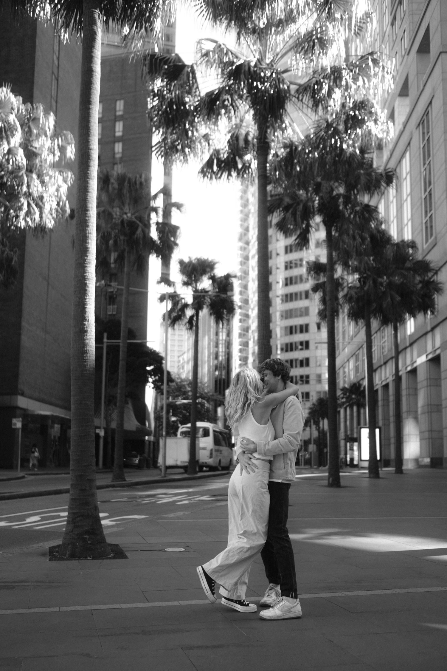 A couple dancing in a city street lined with palm trees and modern buildings.