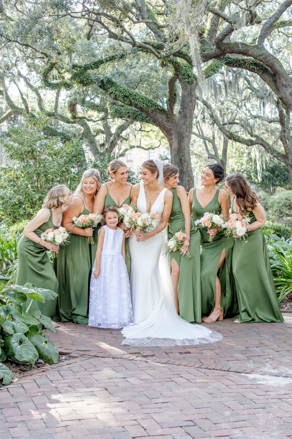Bridal party in sage green dresses poses with bride under moss-draped oak trees.