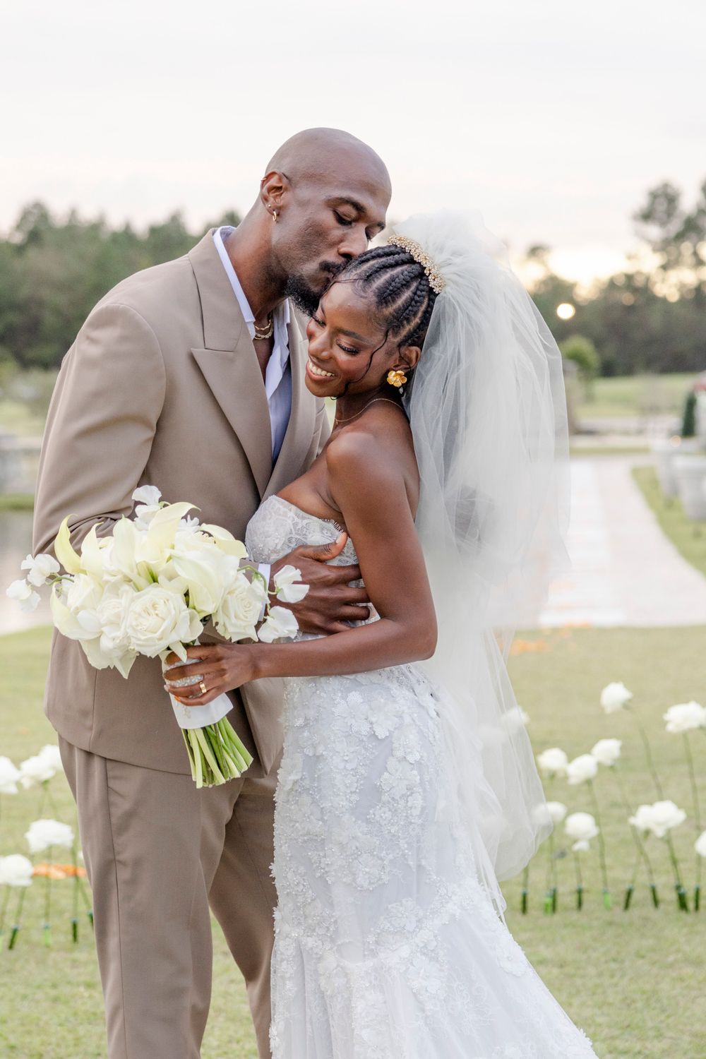A romantic wedding moment captured outdoors with white floral bouquet and beige suit.