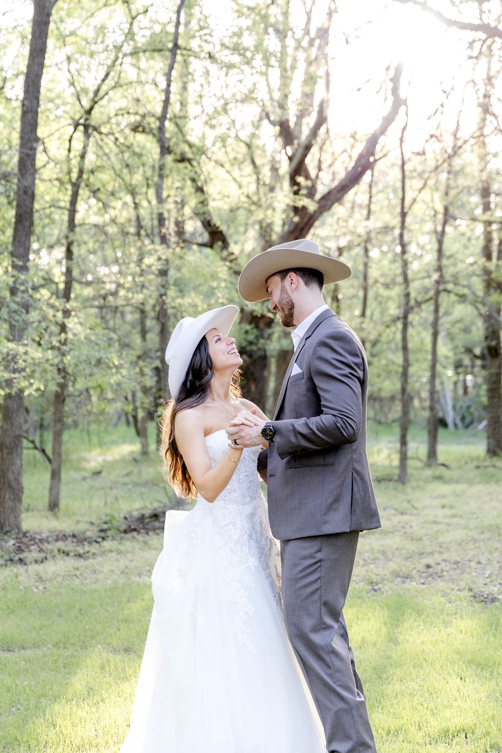 A couple shares their first dance at a wedding ceremony in a sunlit spring forest.