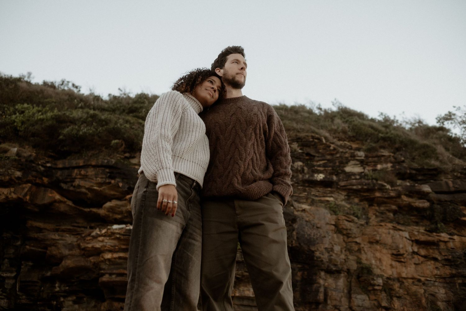 Couple standing on a beach, side by side, looking in to the distance.