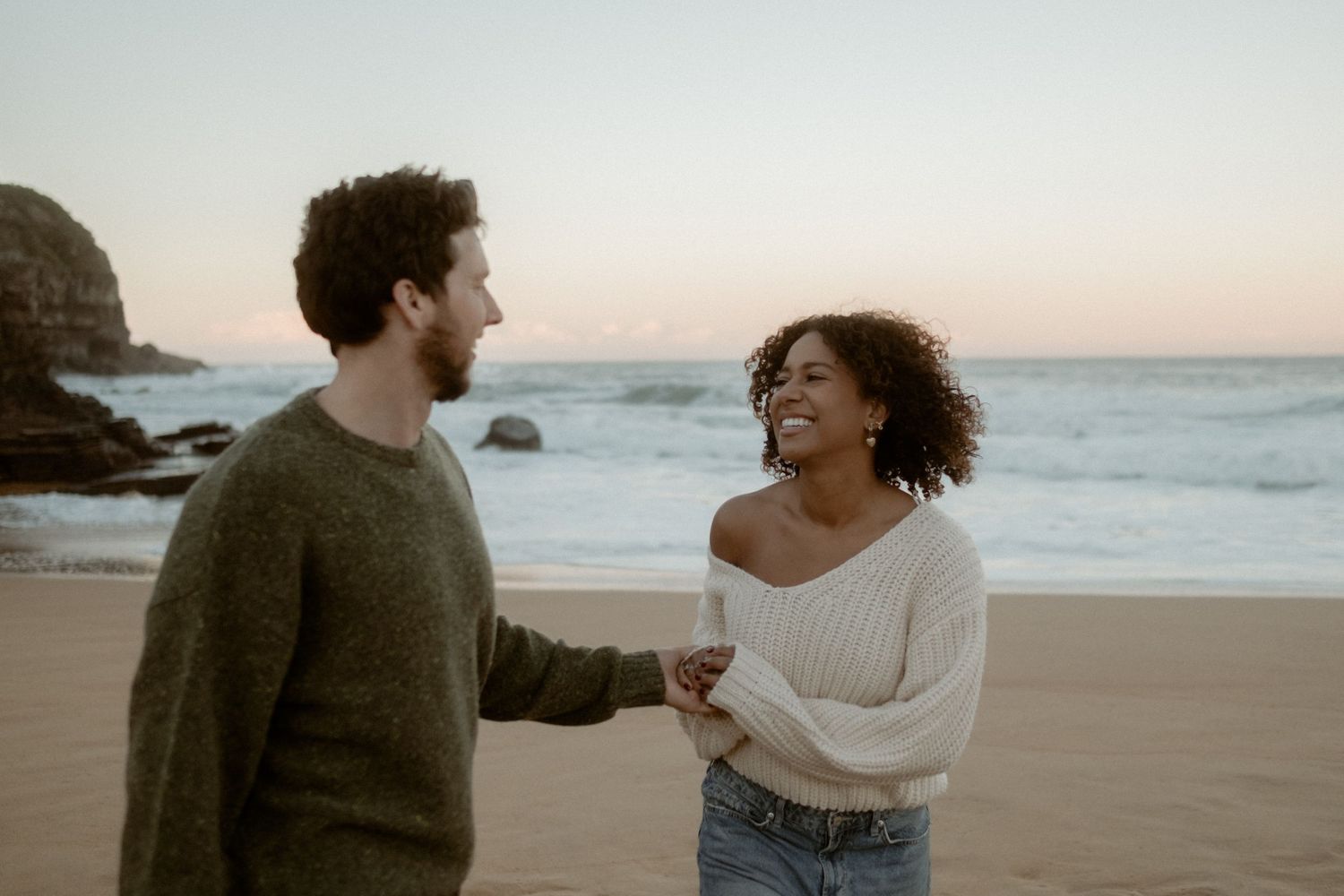 Laughing couple running on a beach with the sun setting in the bachground.