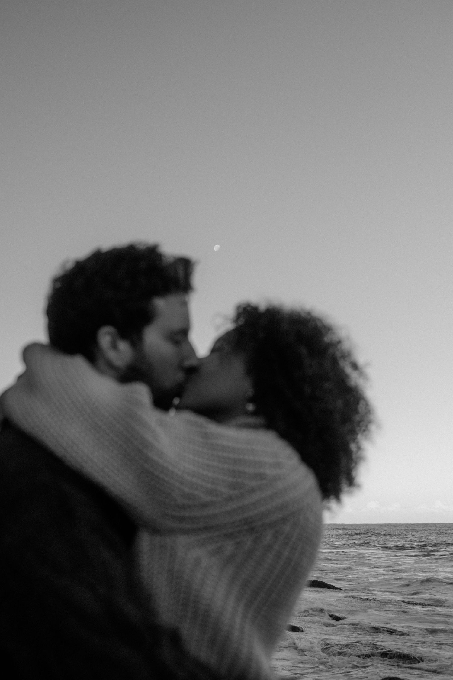 Kissing couple with the ocean and moon behind them.