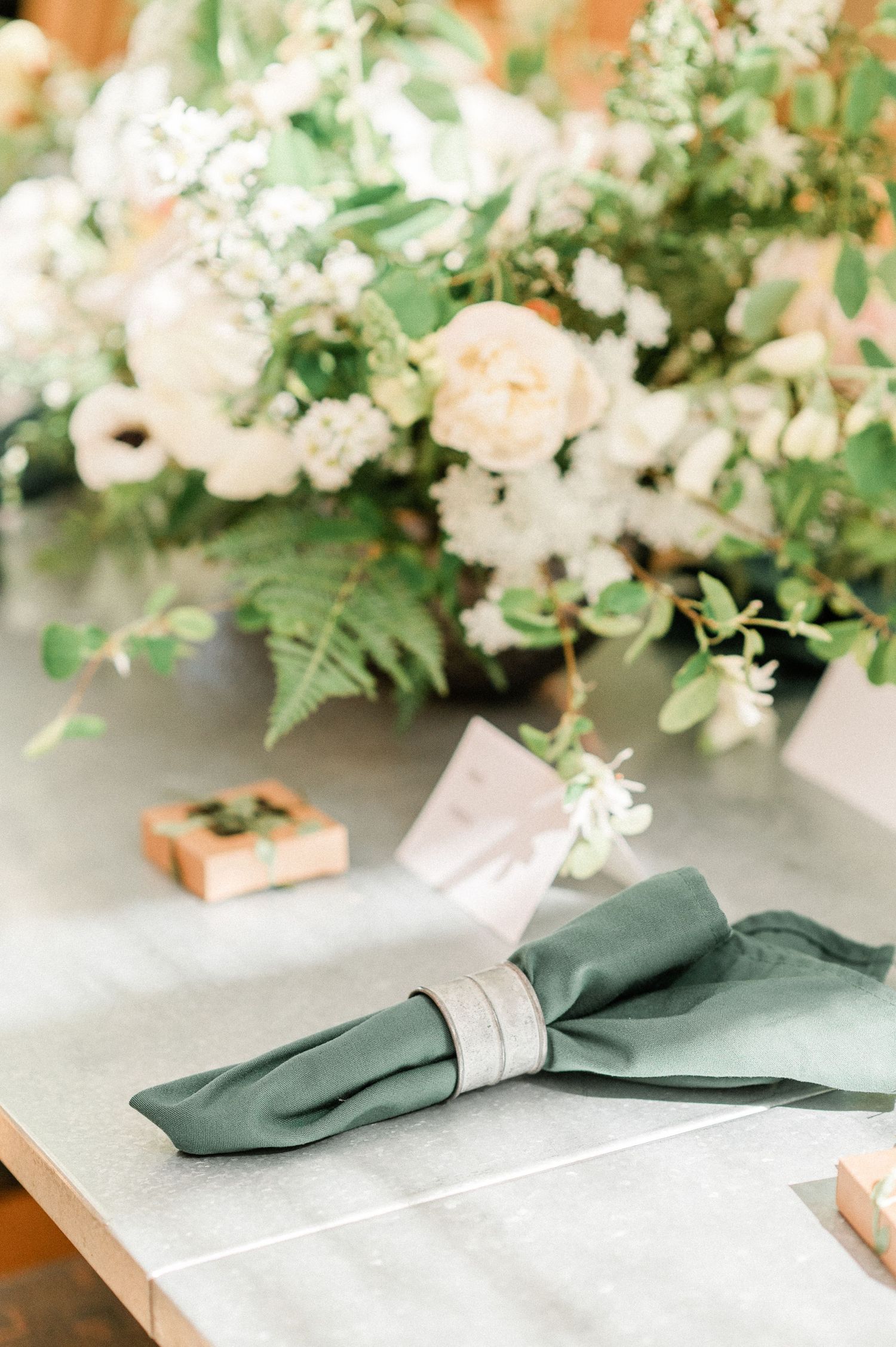 Elegant place settings with forest green napkins and floral arrangements featuring white blooms and greenery on a light surface.