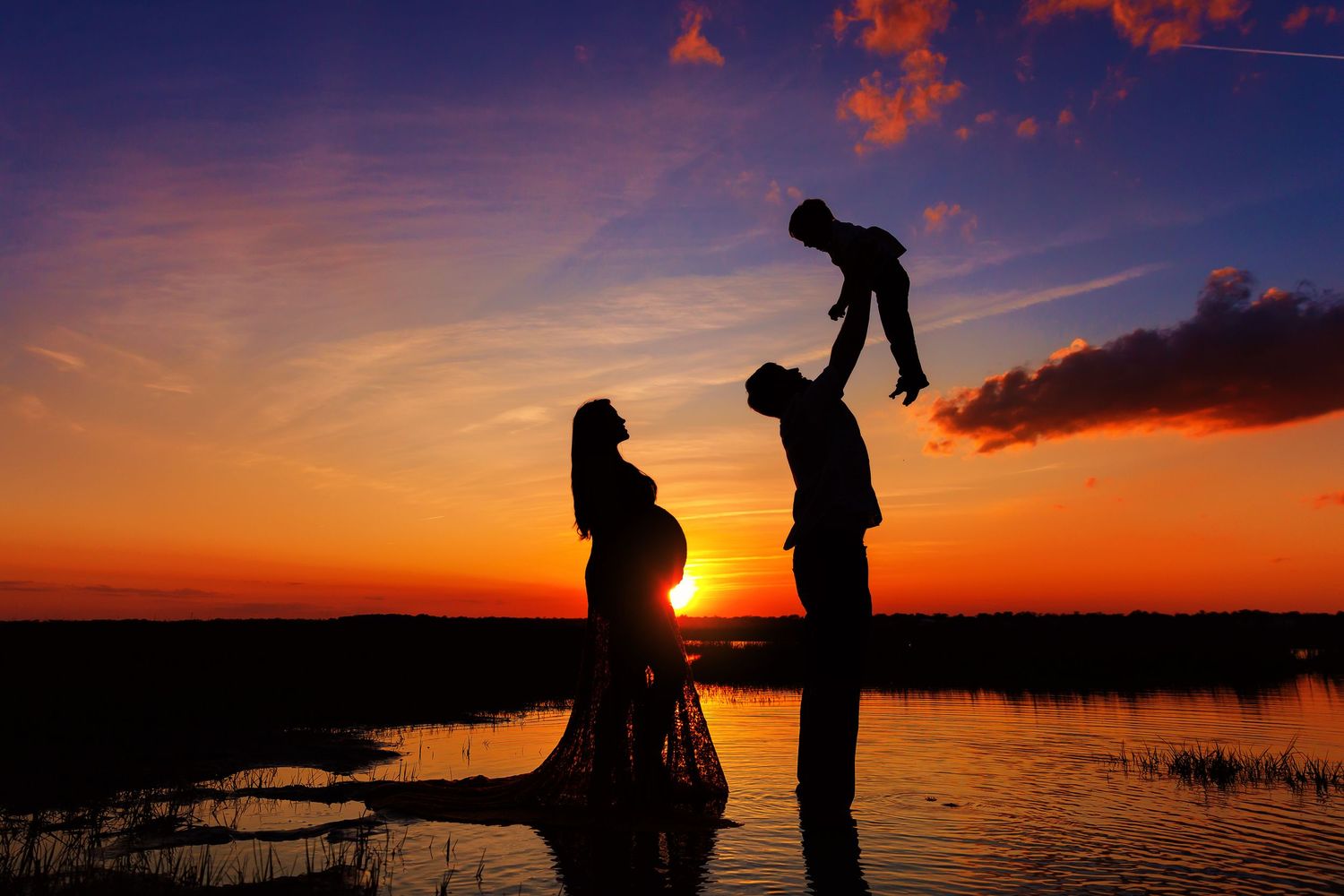 Family silhouettes walking along beach at dramatic purple and orange sunset.