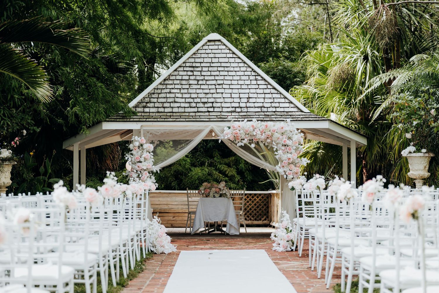 Romantic garden wedding ceremony setup with white chairs and floral arrangements lining the outdoor aisle.