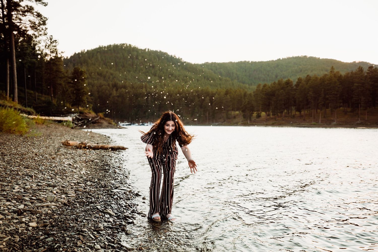 Senior girl in black jumper splashing in lake with mountains in background in South Dakota