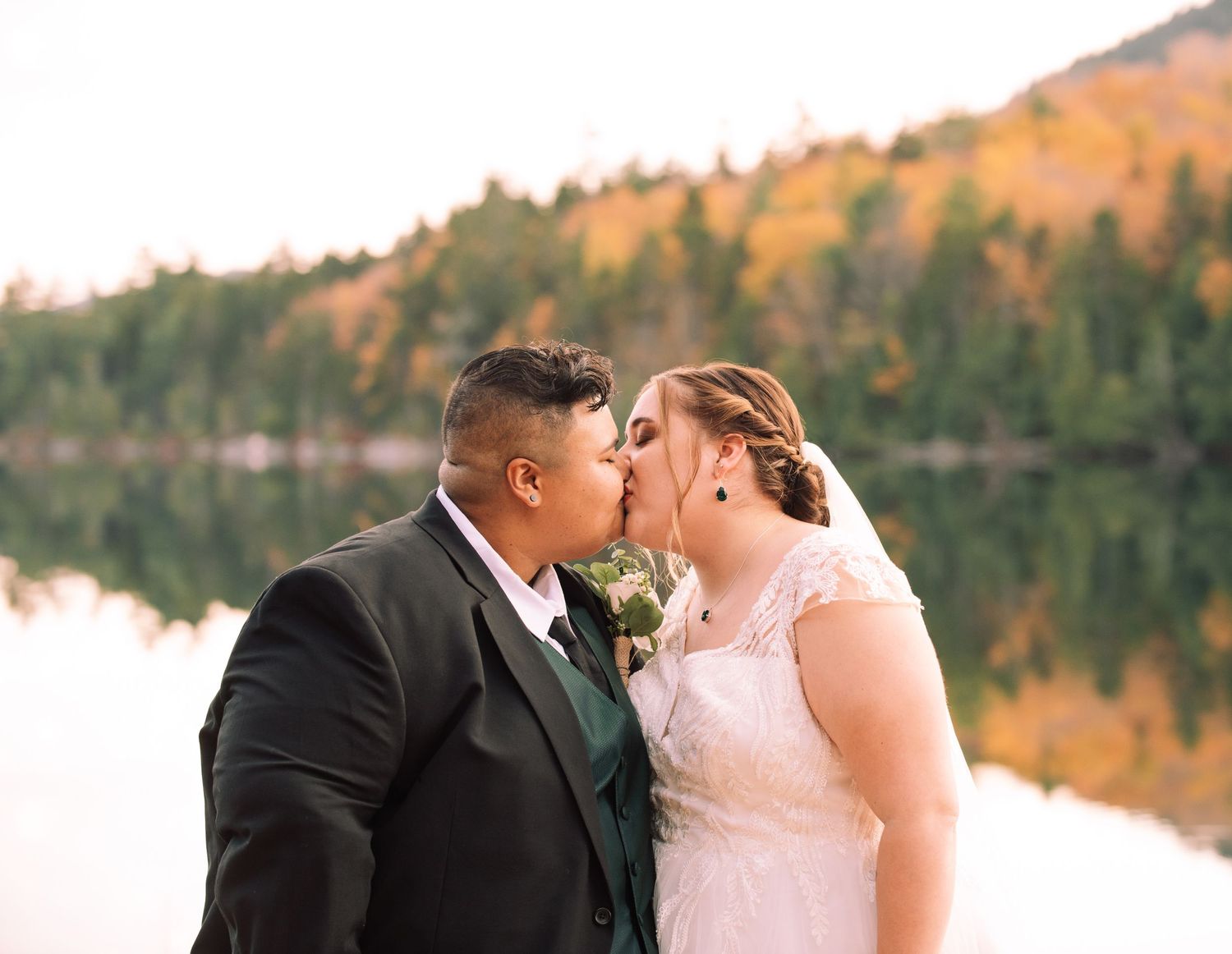 A romantic wedding photo series showing a couple kissing against a scenic autumn backdrop by a lake.