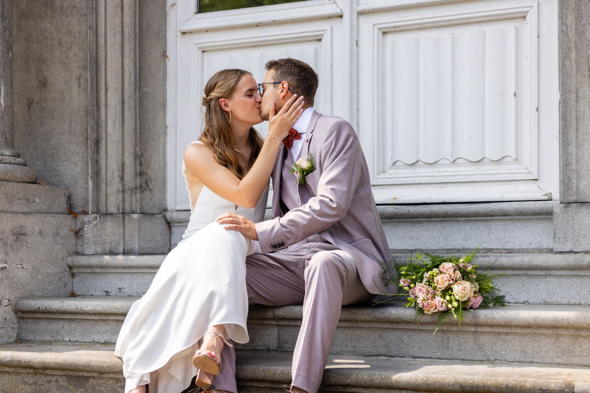 Romantic wedding moment captured on white stone steps with bouquet.