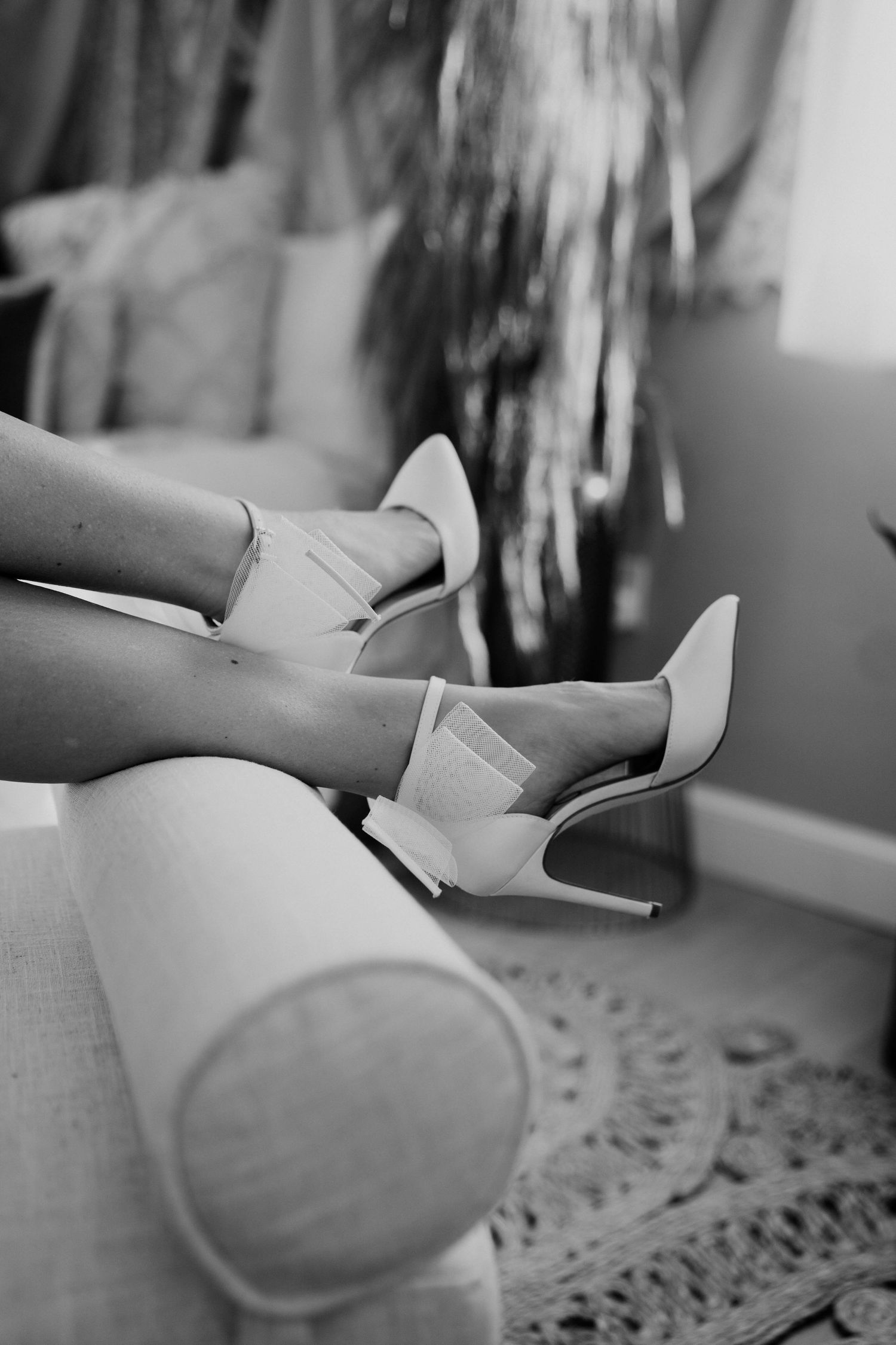 White stiletto heels being worn while lounging on a plush grey couch in a monochromatic setting.