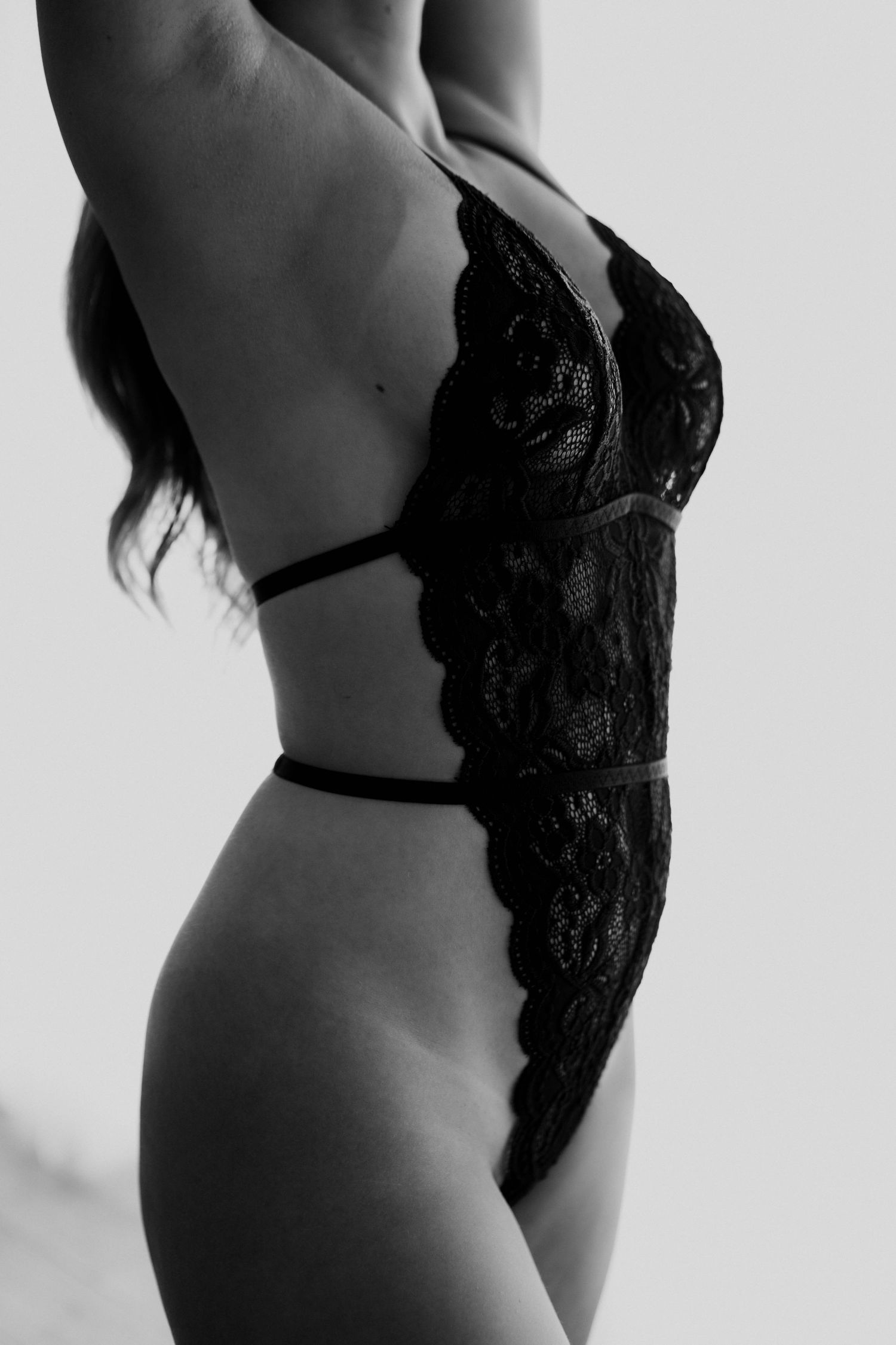 Black and white artistic boudoir photography showing a person in lace lingerie against light background.