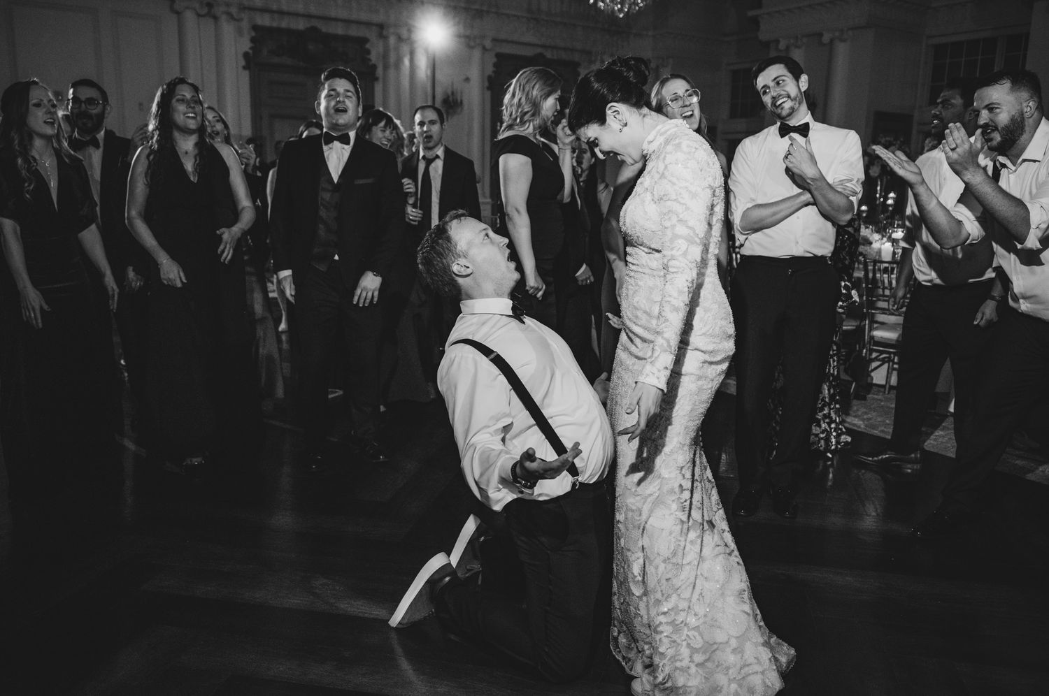 Wedding guests dancing together on a dark dance floor during an evening reception celebration.