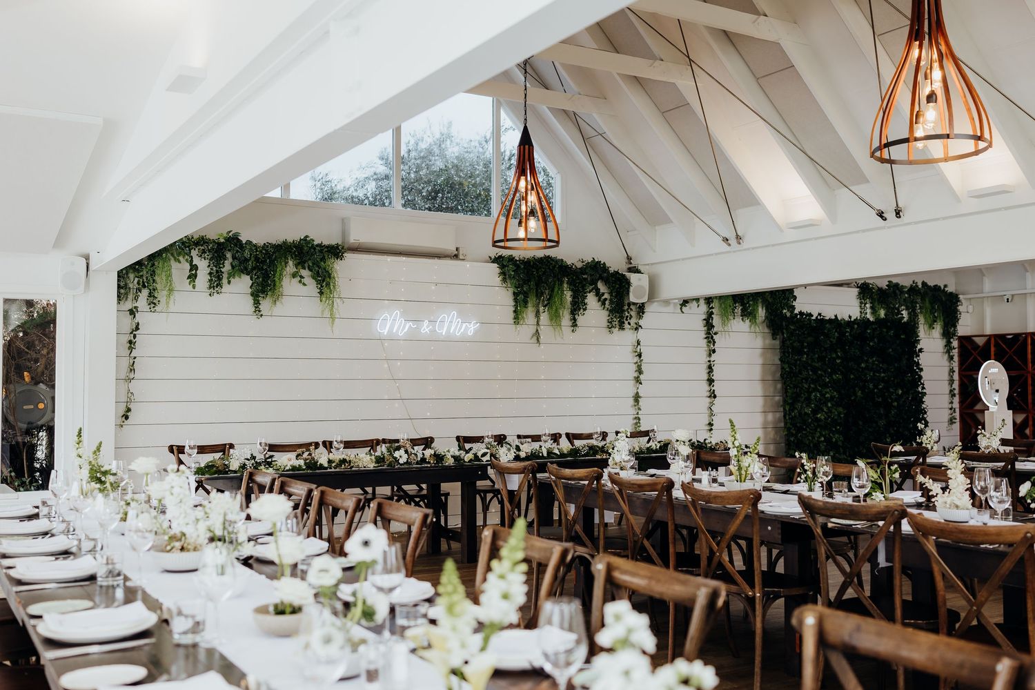 A rustic wedding reception venue with white vaulted ceilings, copper pendant lights, and elegant table settings.