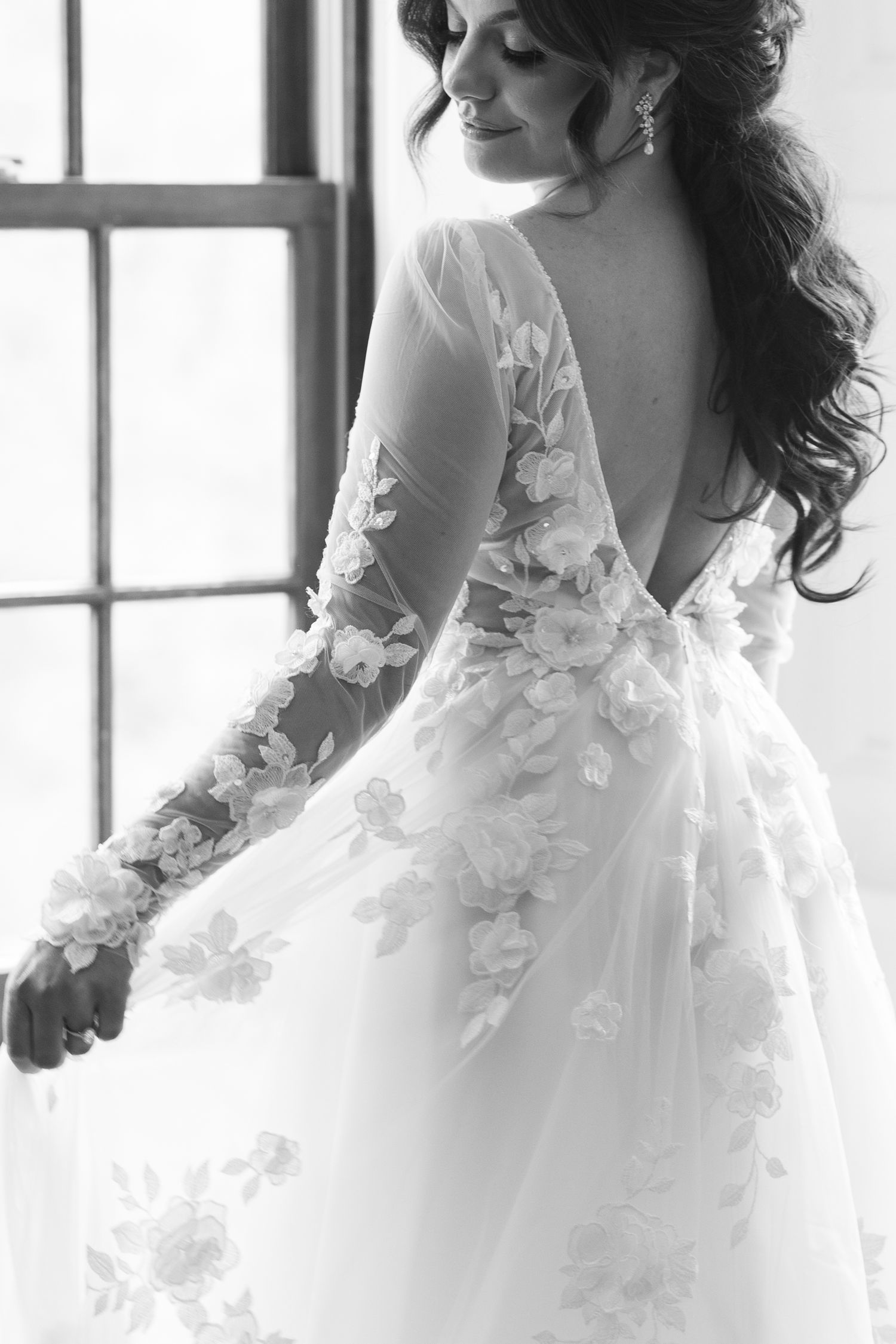Black and white photo of bride in floral applique lace wedding dress with deep V back.