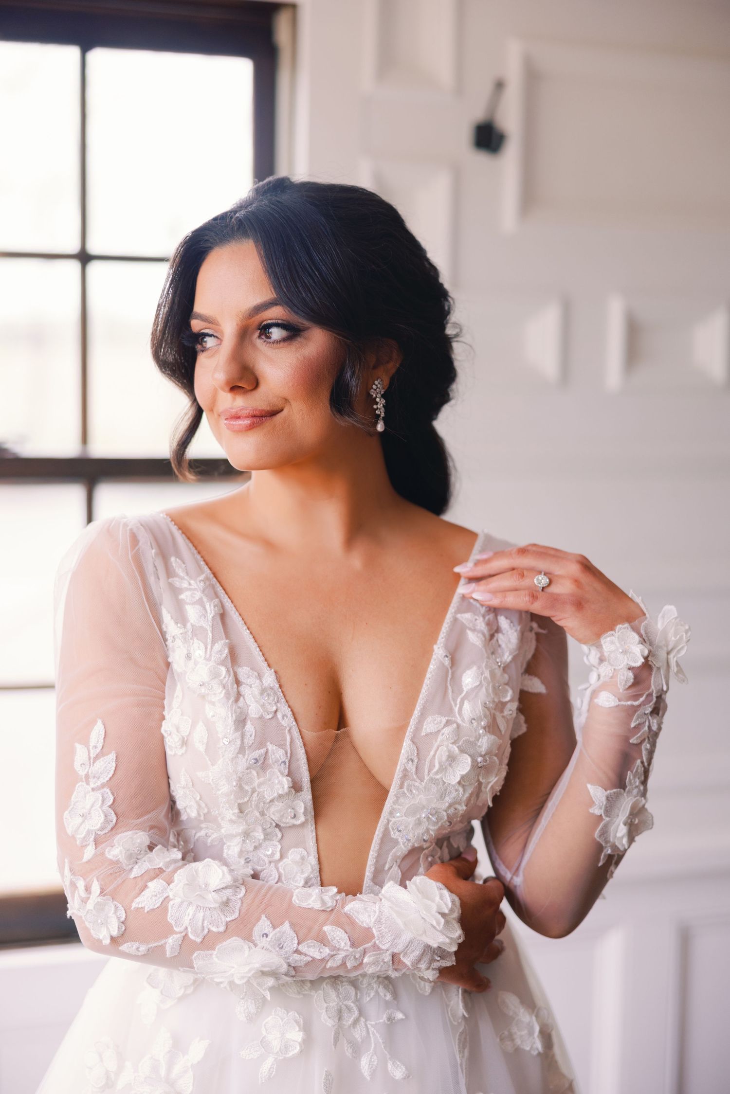 Beautiful bride in floral lace plunge neckline wedding dress with diamond ring and earrings.