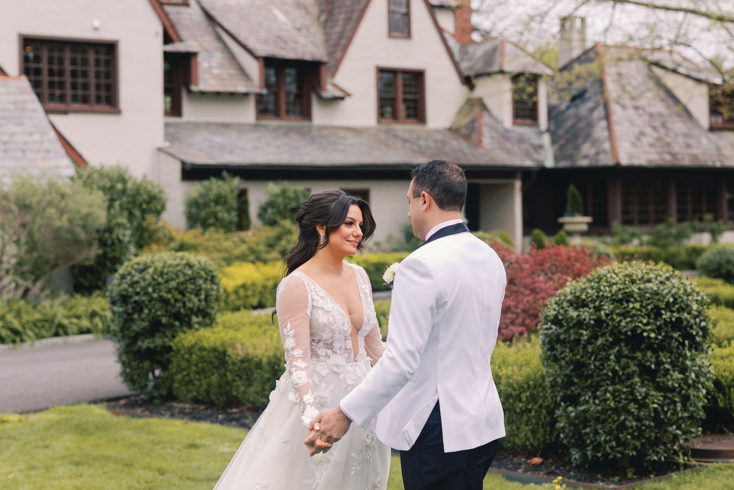 Bride and groom holding hands and smiling at each other in a lush garden setting.