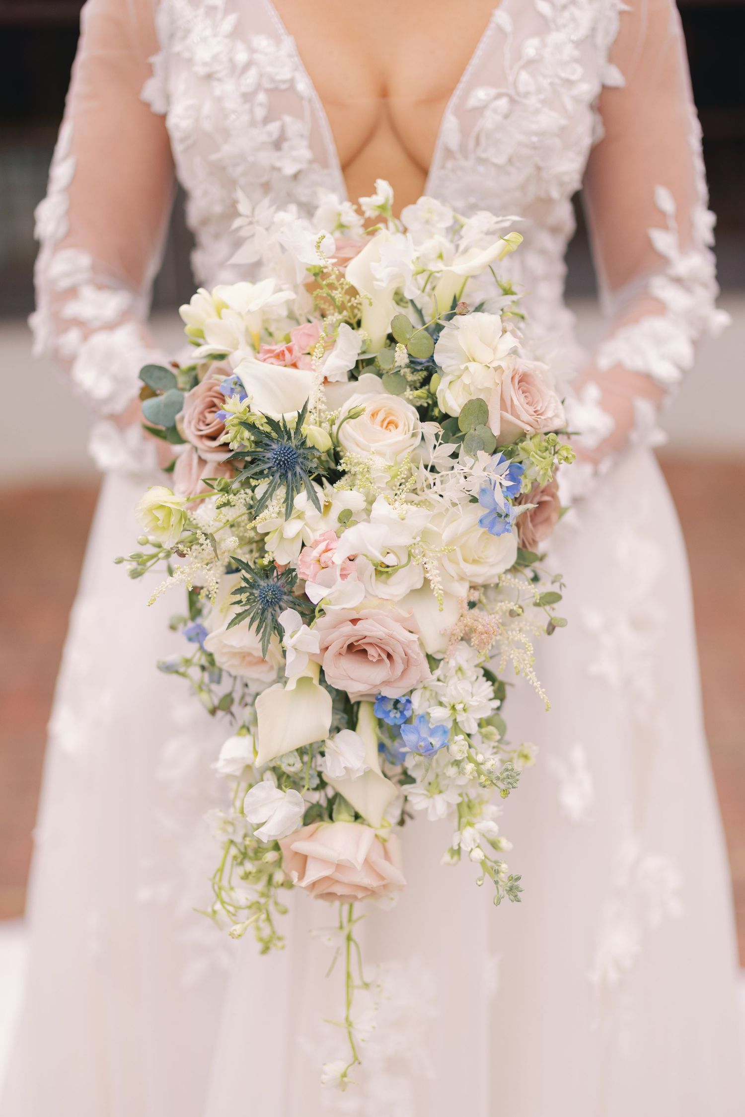 Close-up of a cascading bridal bouquet with blush roses, white blooms, and blue flowers.