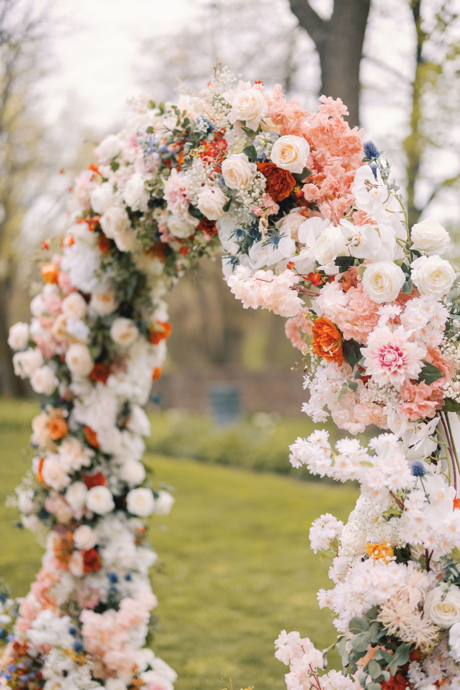 Stunning circular wedding arch covered in white, pink, and orange blooms in an outdoor garden setting.