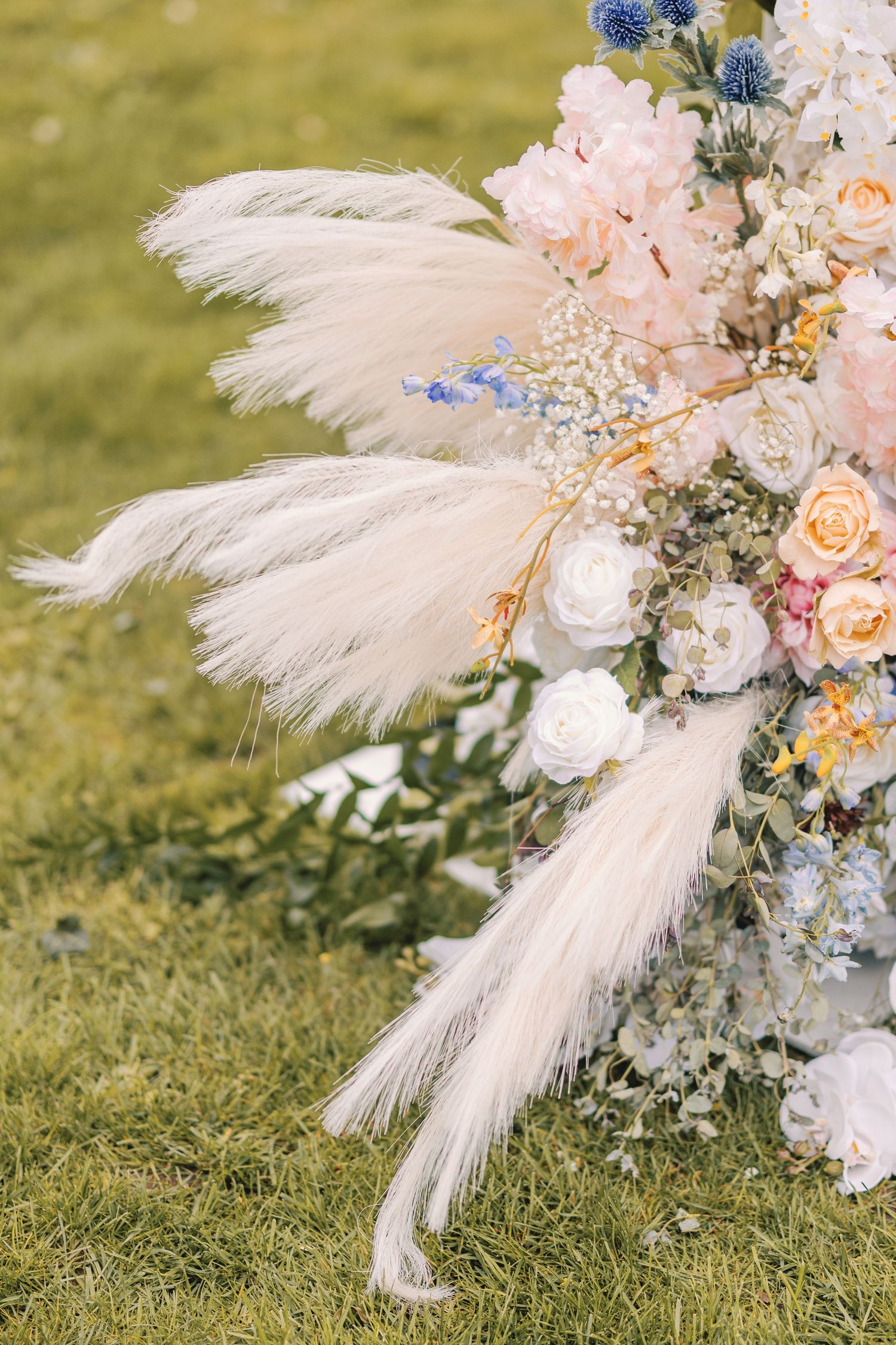 Wedding arch detail with white pampas grass plumes and pastel pink, cream, and blue floral arrangement.