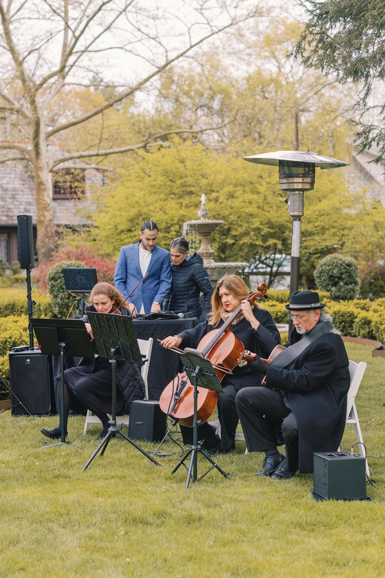 String quartet performing outdoors at a garden wedding ceremony with lush green landscaping in background.