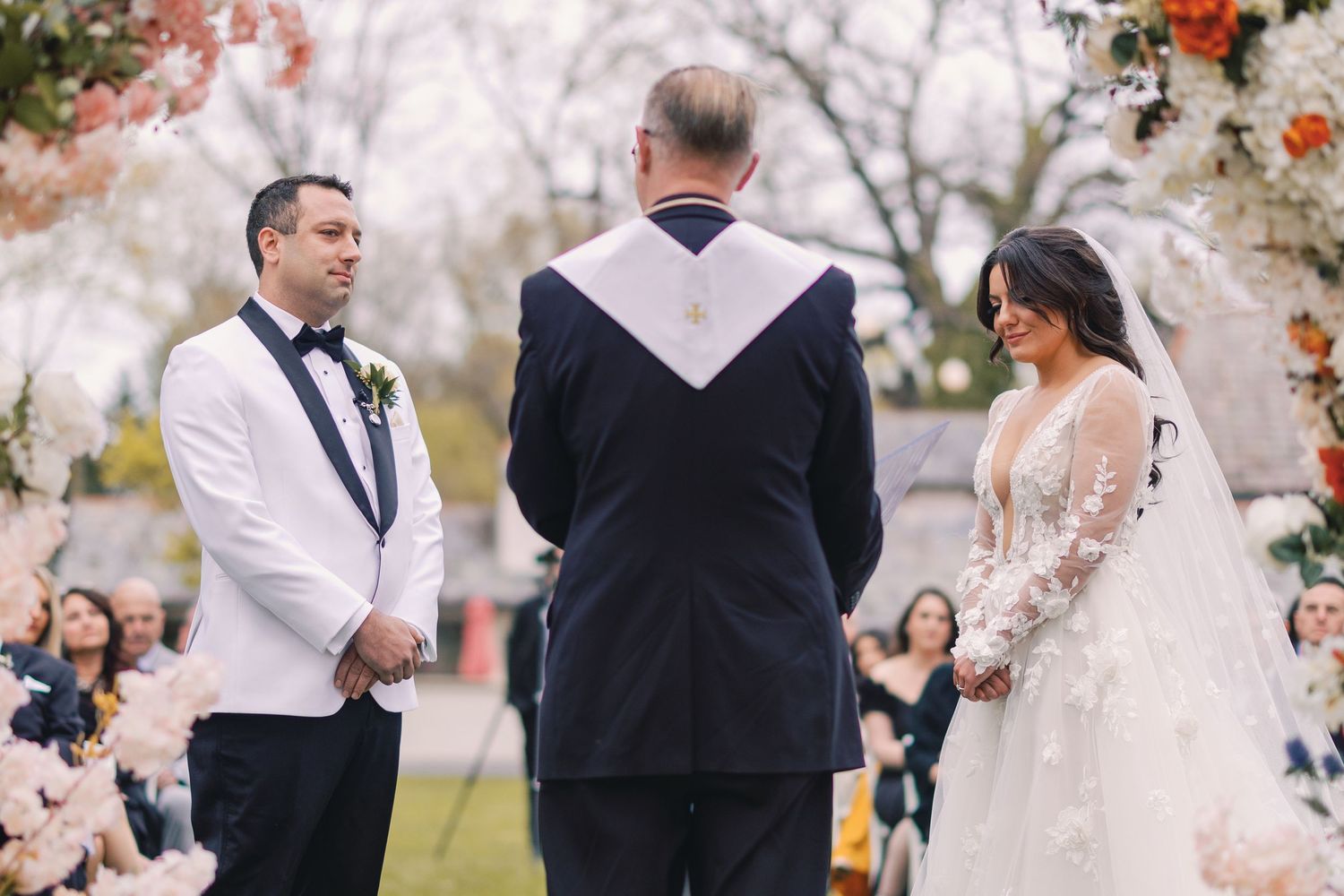Bride and groom exchange vows at outdoor wedding ceremony with floral arch and officiant.