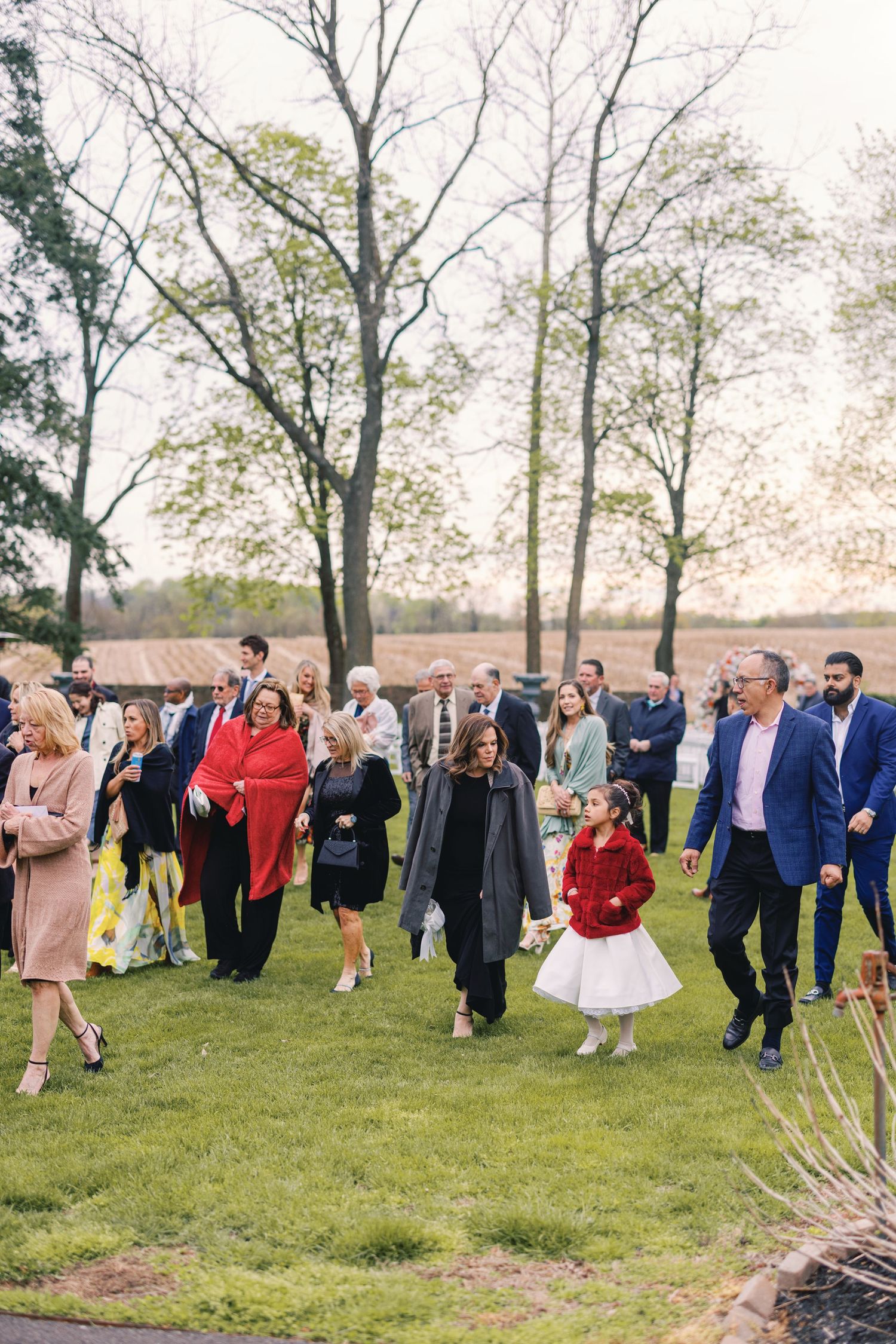 Wedding guests walk across green lawn at outdoor reception venue at dusk.